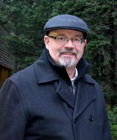 a middle-aged white man with a black and white goatee wearing glasses and a black coat smiling at the camera
