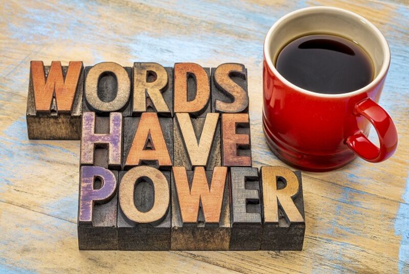 Wooden letter blocks laid out to read: Words Have Power, on a table with a red coffee mug.