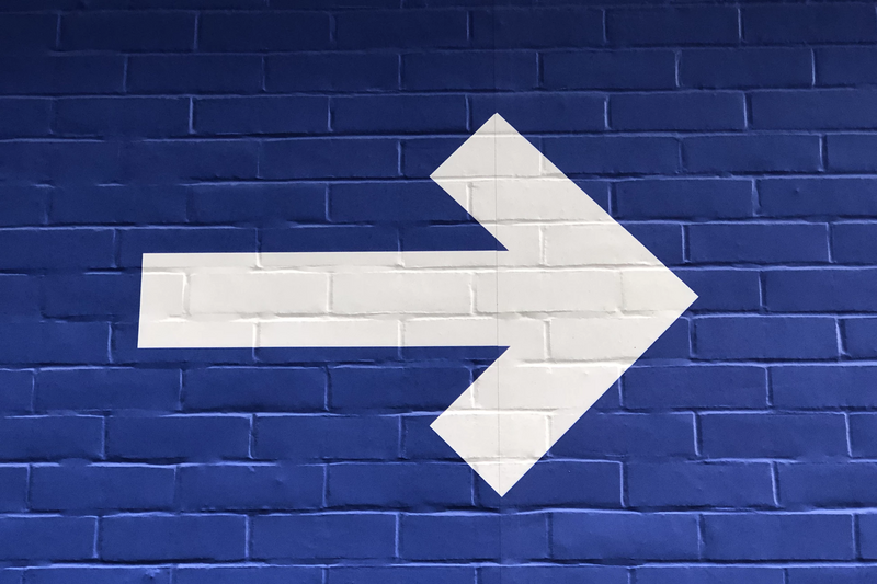 White arrow painted on blue brick wall.