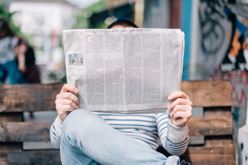 A man sitting on a bench reading the newspaper.