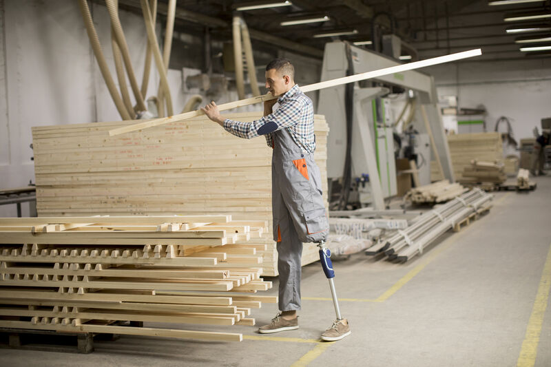 Man with a prosthetic leg at work carrying lumber.