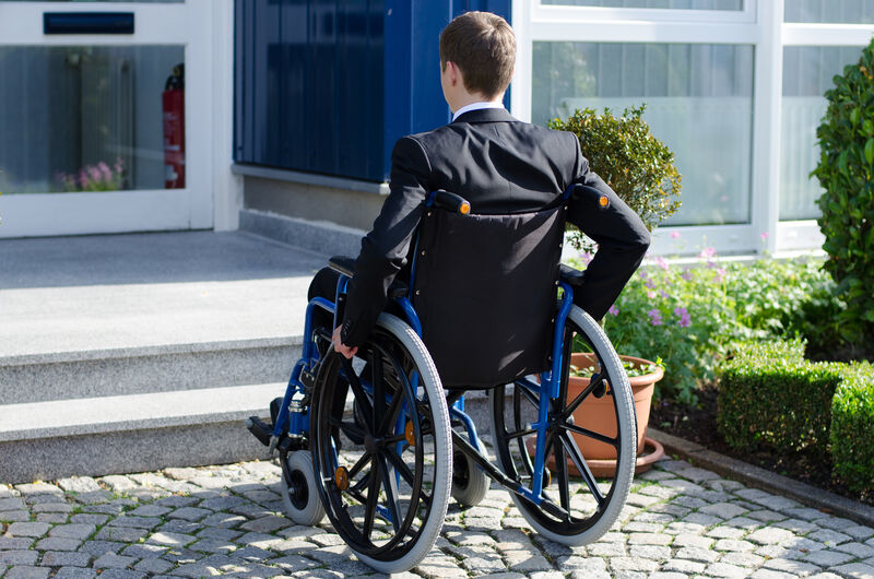 A man in a wheelchair facing a flight of stairs.