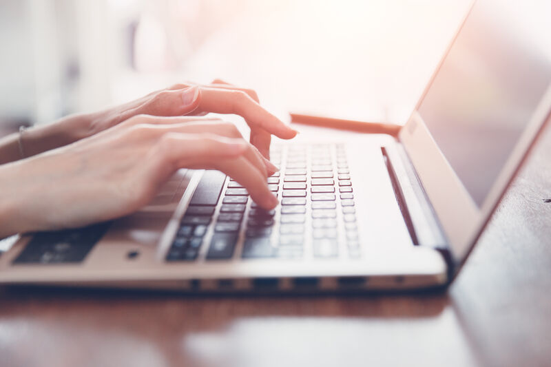 Close up of a person typing on a laptop that is sitting on top of a wooden desk.