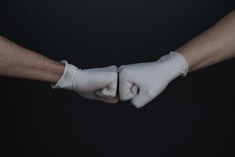 Two hands fist bump in solidarity, with gloves on.