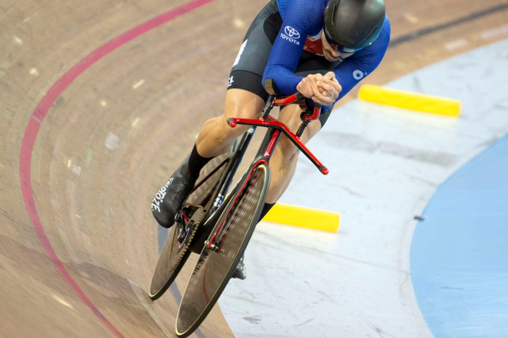 The blog author racing his track bike on a banked wooden track, hunched over in an aerodynamic position. 