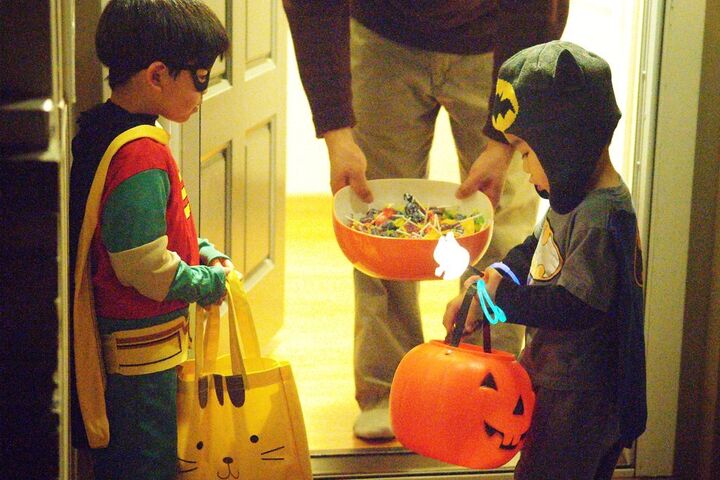 Two children dressed in Halloween costumes are receiving Halloween candy at  someone's front door.  