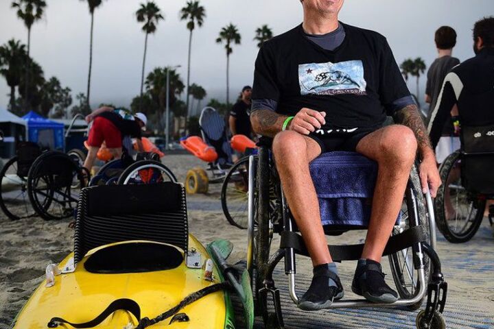 Charles Webb in his wheelchair next to an adaptive surfboard.