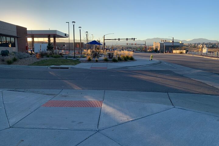 A recently completed project of an accessible curb ramp/crosswalk taken at sunset with commerce, residential neighborhoods, and mountains leading to the horizon.