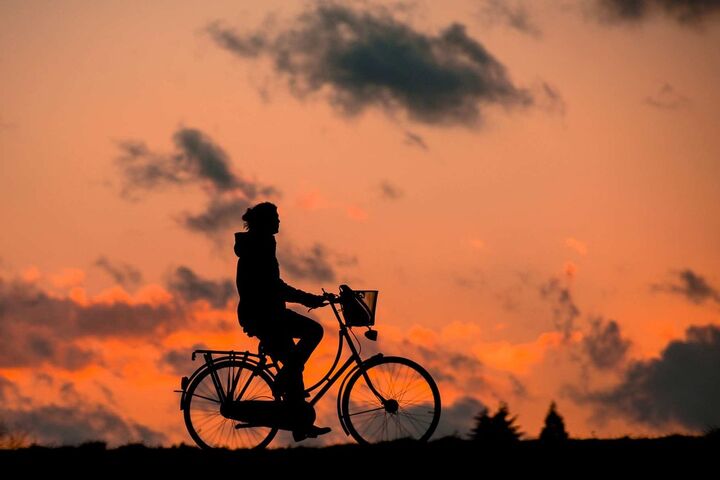 Silhouette of a person on a bike, with a sunset background.