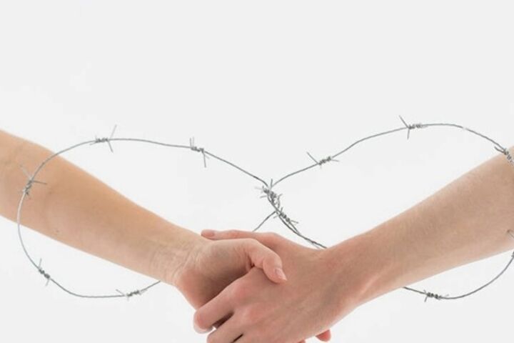 Two hands connecting through a barbed wire.